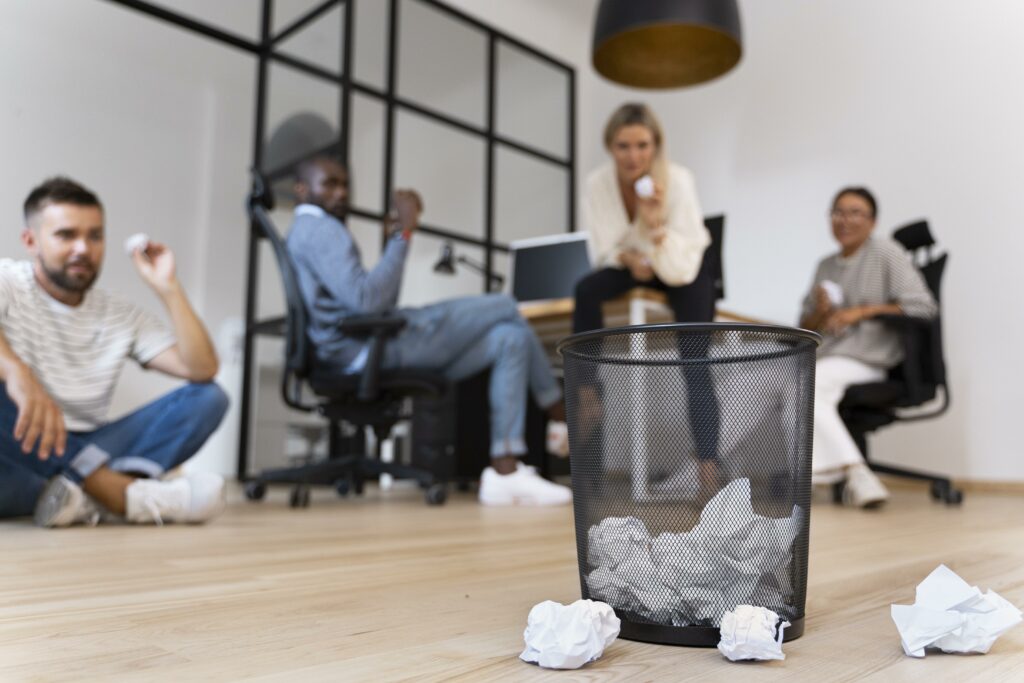 Quatre employées de bureau, jetant des boulettes de papier dans une corbeille noire, pour montrer l'importance d'une gestion des déchets efficace.